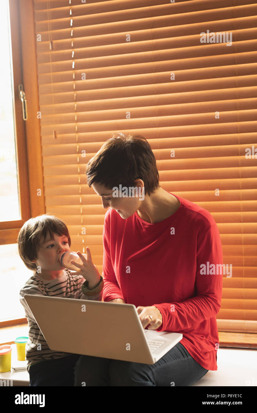 La mère et le fils assis avec un ordinateur portable à la maison Banque D'Images