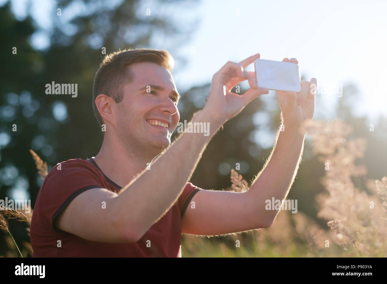 Young man holding mobile phone dans les mains au coucher du soleil de prendre une photo de la nature sur le téléphone. Banque D'Images
