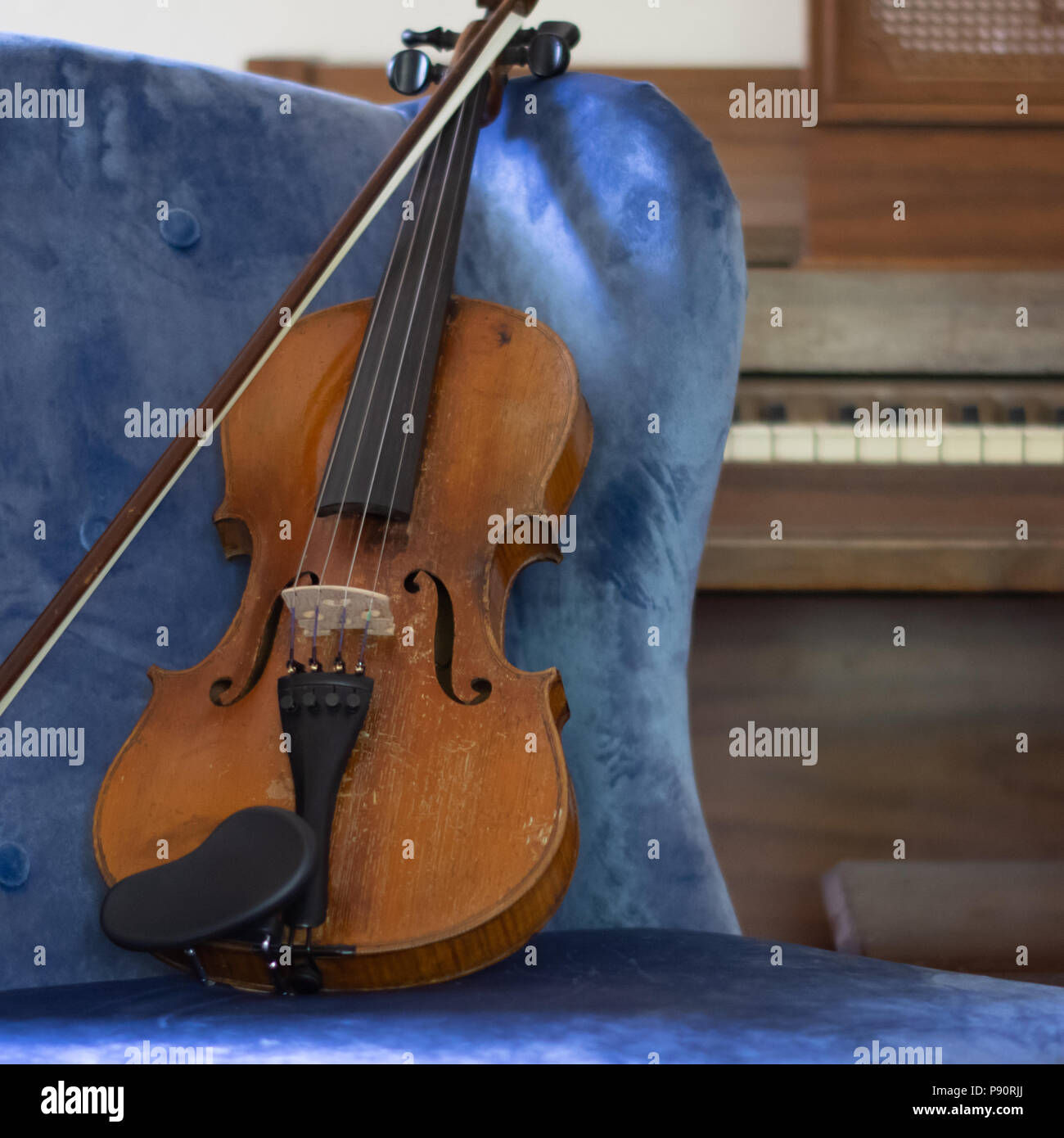 Violin and Bow reposant en bleu chaise avec piano en arrière-plan Banque D'Images