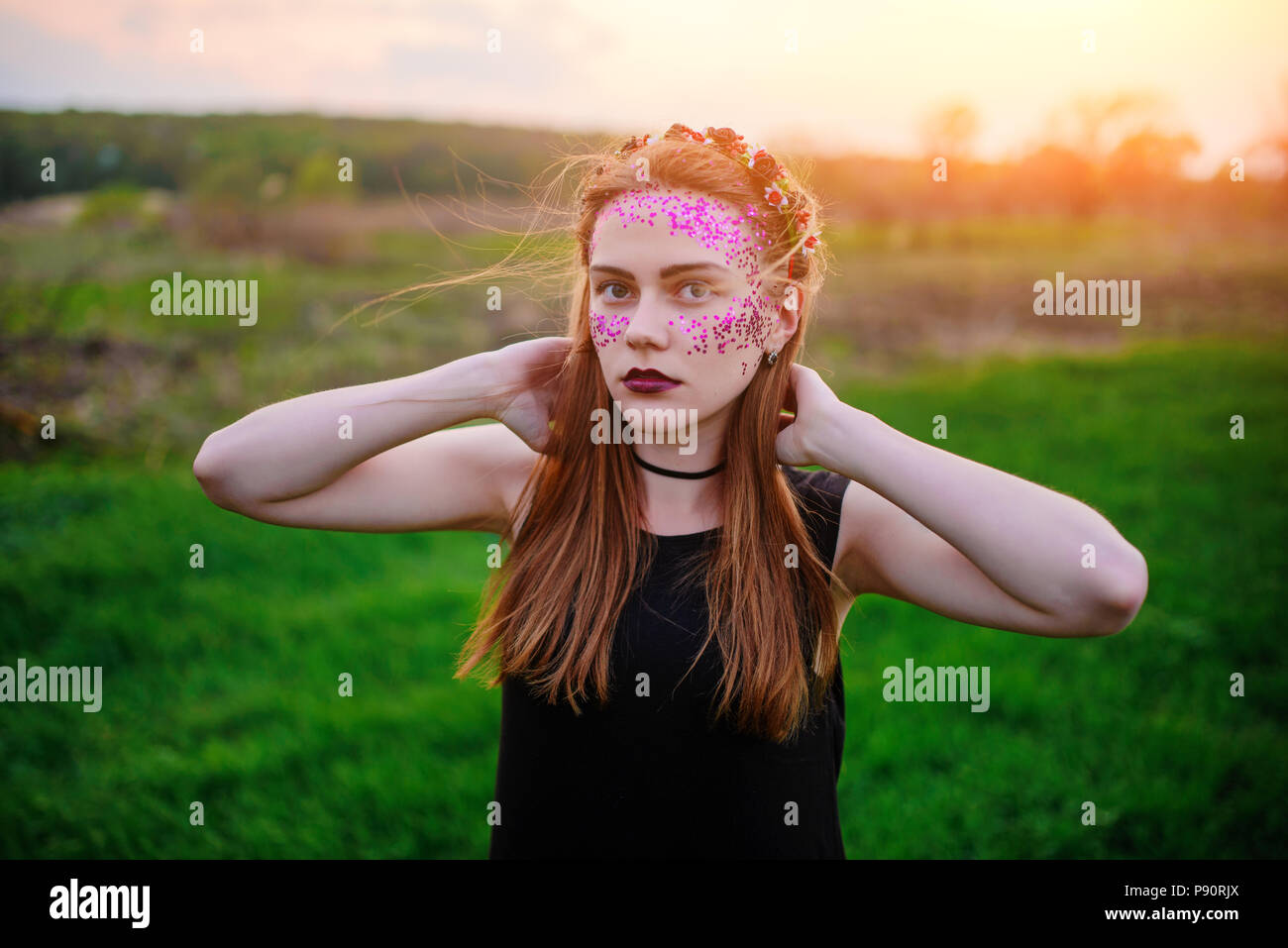 Une belle jeune femme avec un éclat violet sur son visage debout sur l'herbe et regardant la caméra. Banque D'Images