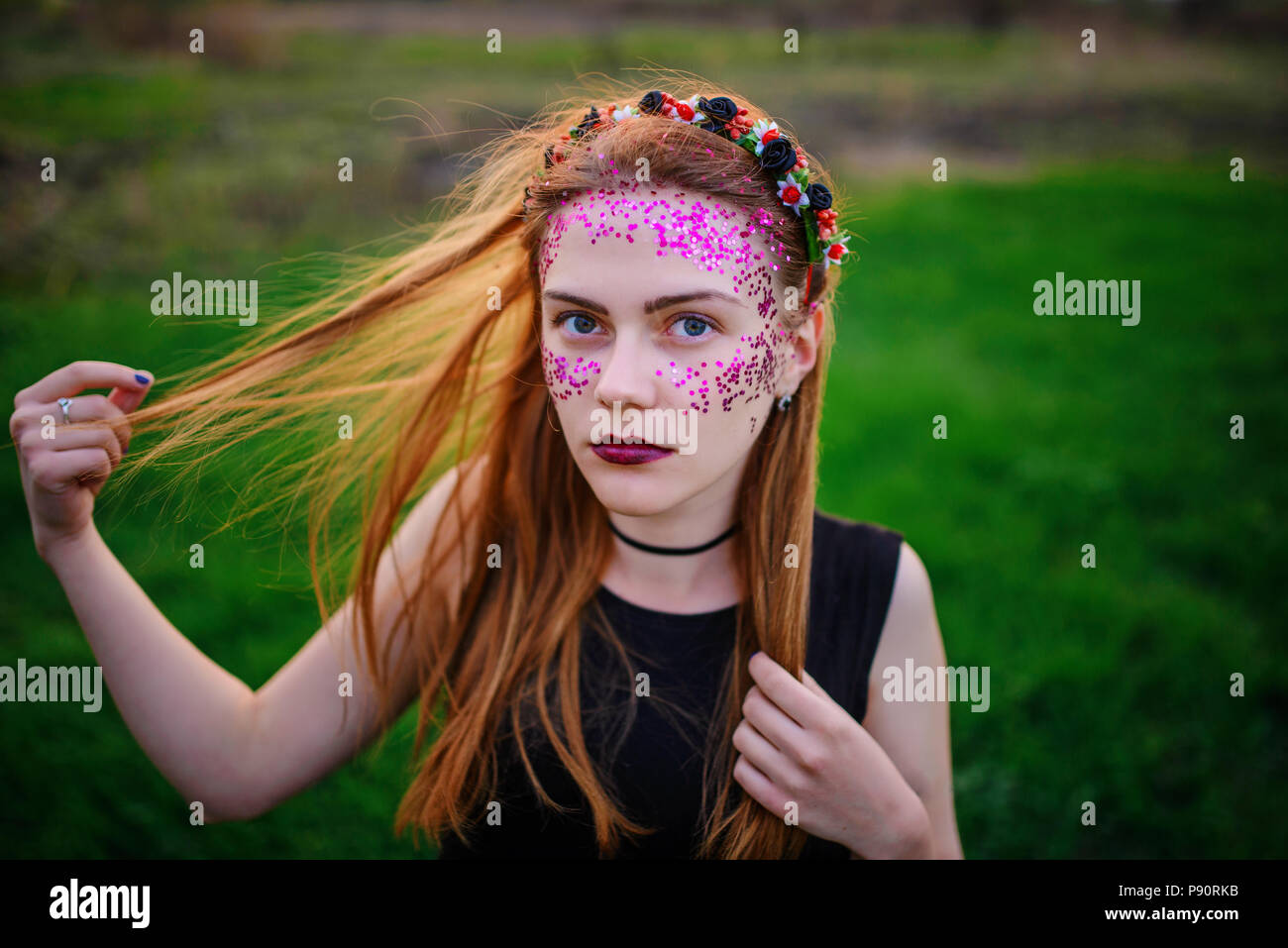 Une belle jeune femme avec un éclat violet sur son visage debout sur l'herbe et regardant la caméra. Banque D'Images