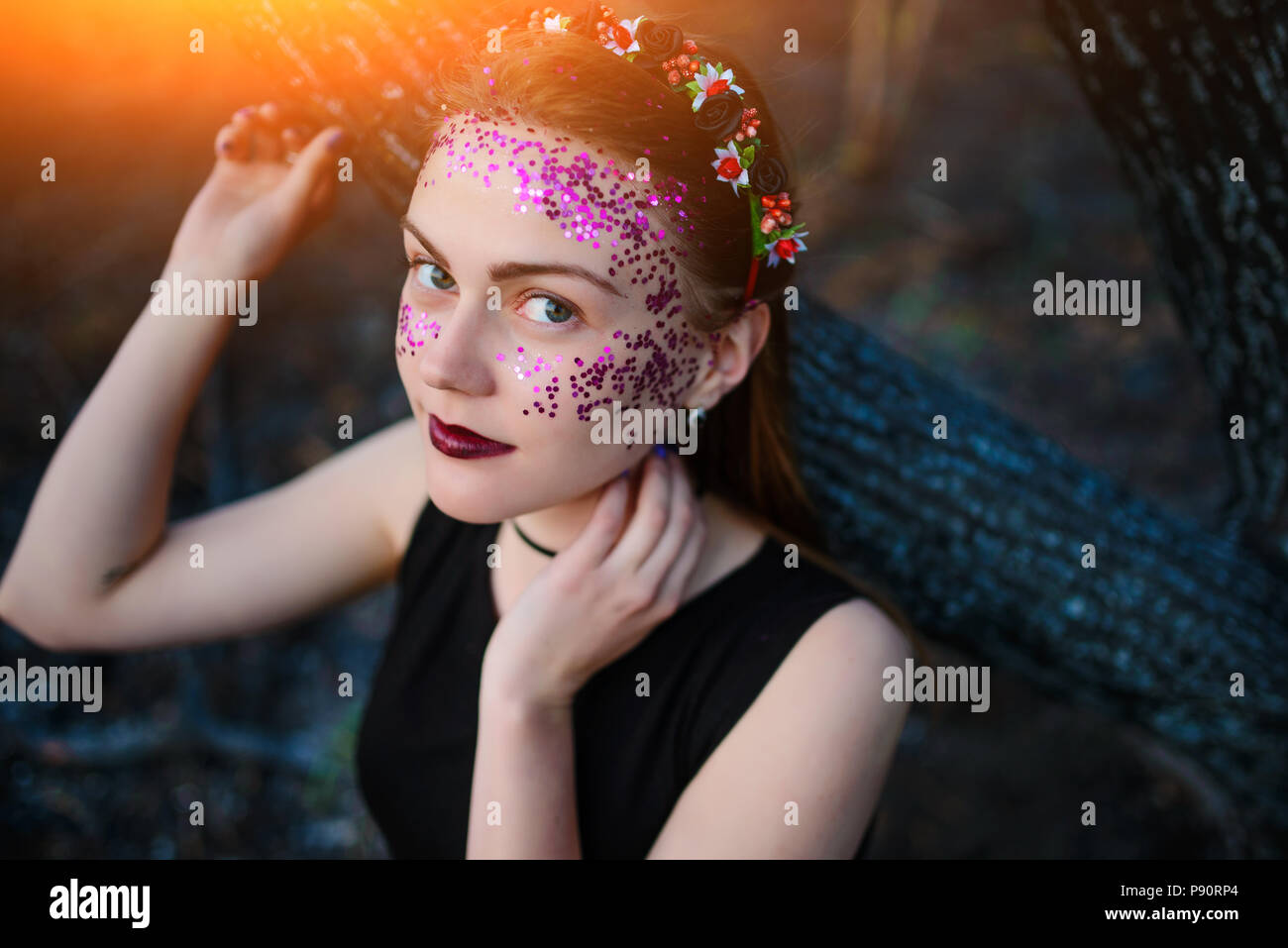 Une belle jeune femme avec un éclat violet sur son visage se tient près d'un arbre brûlé. Banque D'Images