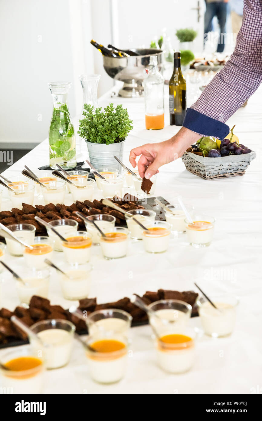 L'homme prenant Brownies sur Buffet Table avec nappe blanche Banque D'Images