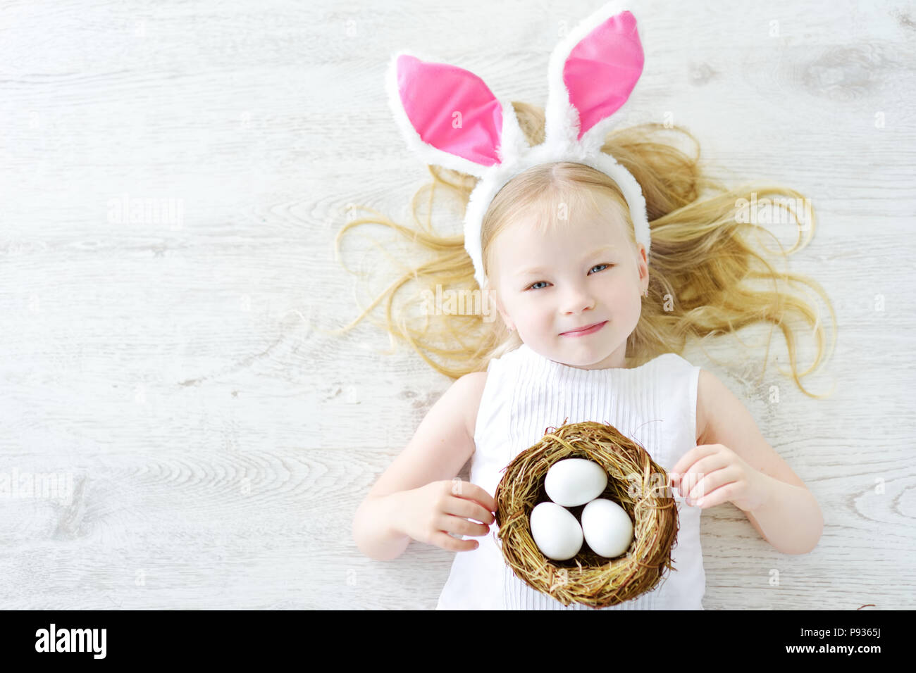 Cute little girl wearing Bunny Ears jouant sur la chasse aux œufs de Pâques. Adorable enfant célébrer Pâques à la maison. Banque D'Images