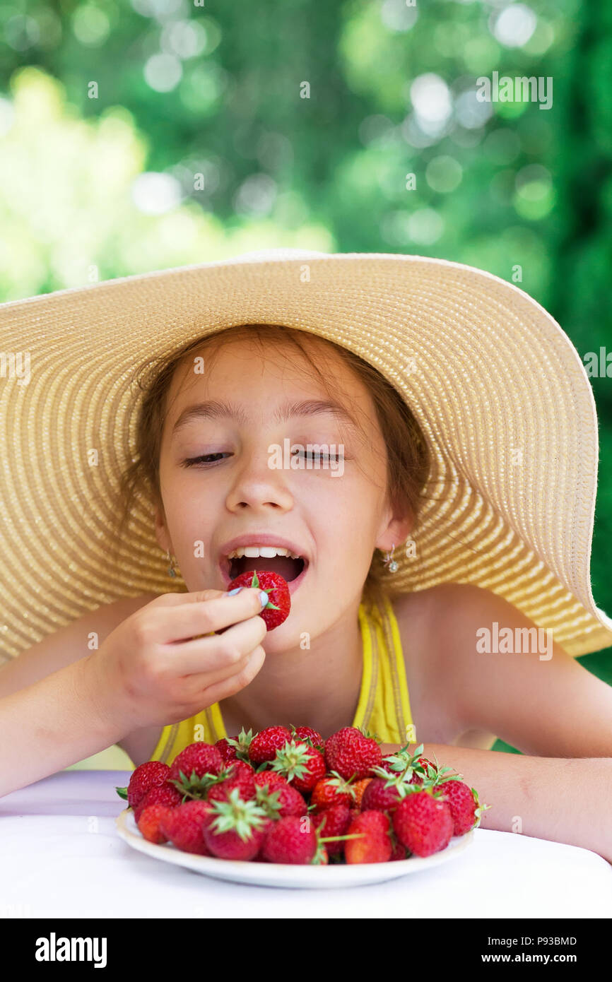 Portrait of cute teen girl in big hat eating strawberry est à jour d'été Banque D'Images