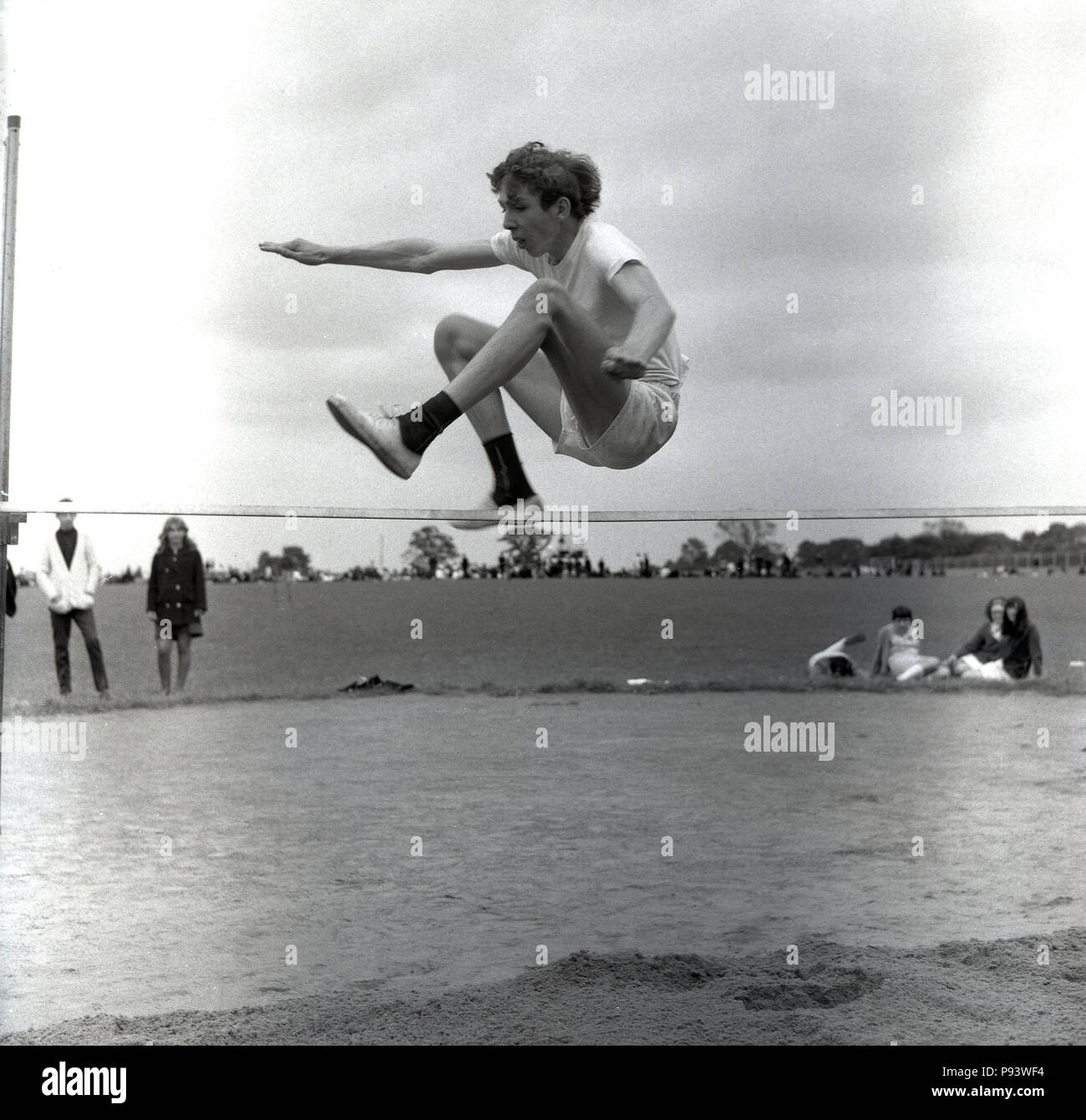 Années 1960, historique, à la mi-air, un jeune garçon sautant ou sauter par dessus une barre du saut en hauteur dans une école des sports jour, England, UK. Banque D'Images