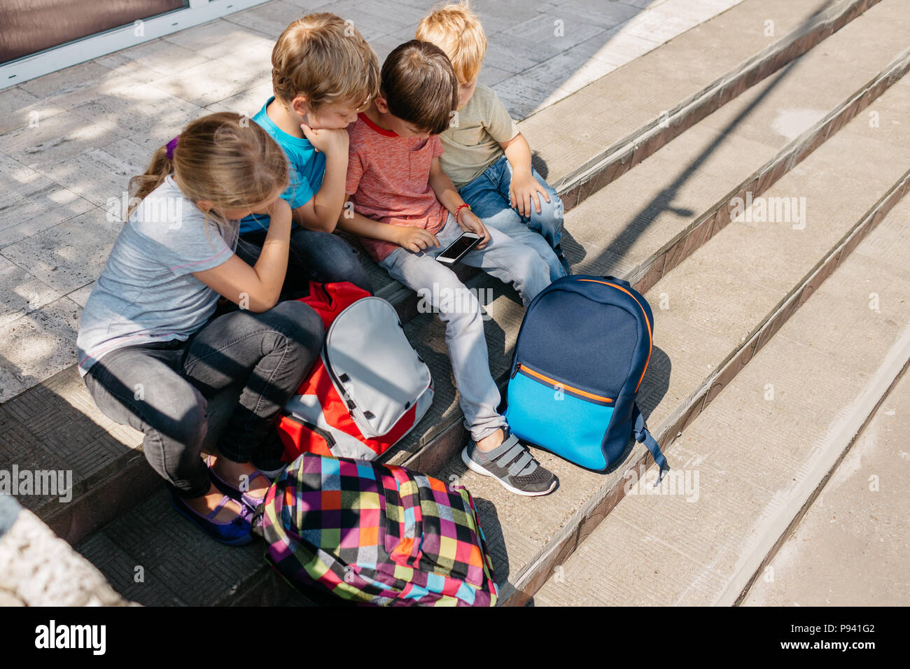 Vue de dessus de l'école des enfants assis sur des escaliers en jouant avec un mobile. Les enfants jouent sur un téléphone cellulaire pendant les congés scolaires. Banque D'Images