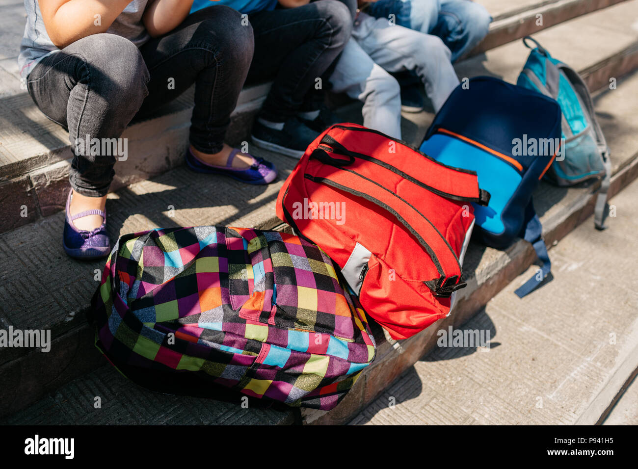 Image recadrée de sacs d'école dans des escaliers. Groupe d'étudiants assis sur les escaliers à l'extérieur de l'école avec leurs sacs à dos en face d'eux. Banque D'Images
