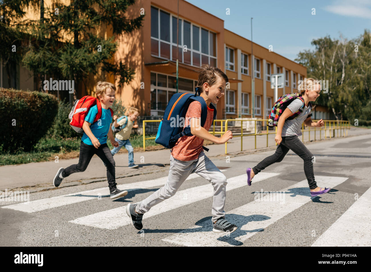 Groupe de camarades rire se précipiter hors de l'école crossing road. Heureux les enfants qui traversent une route à un passage pour piétons. Banque D'Images
