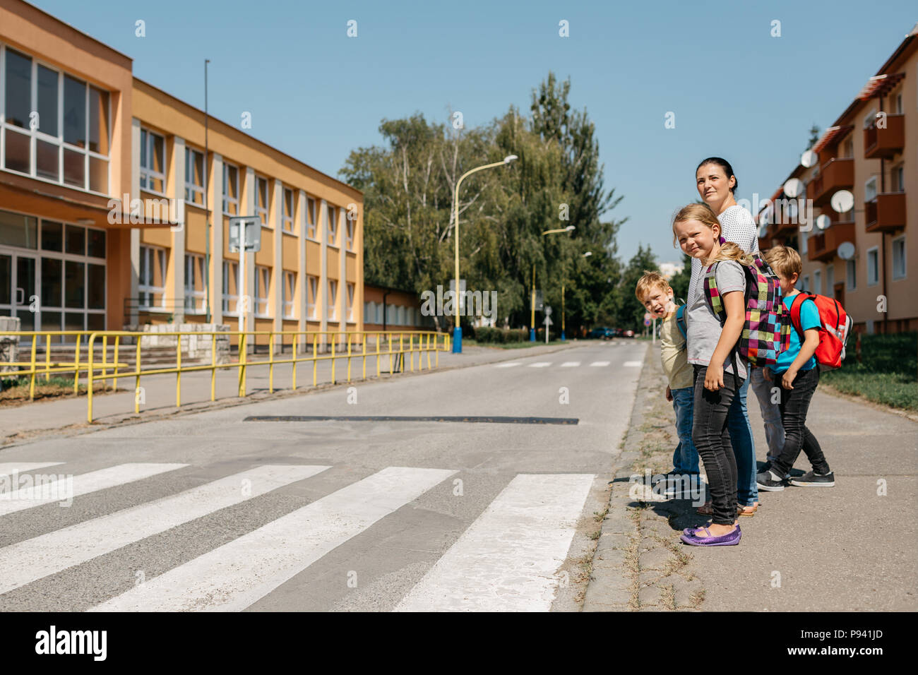 Mère à l'école à pied avec ses enfants en leur enseignant la sécurité routière. Les enfants sur le chemin de l'école attendant à un passage pour piétons. Banque D'Images