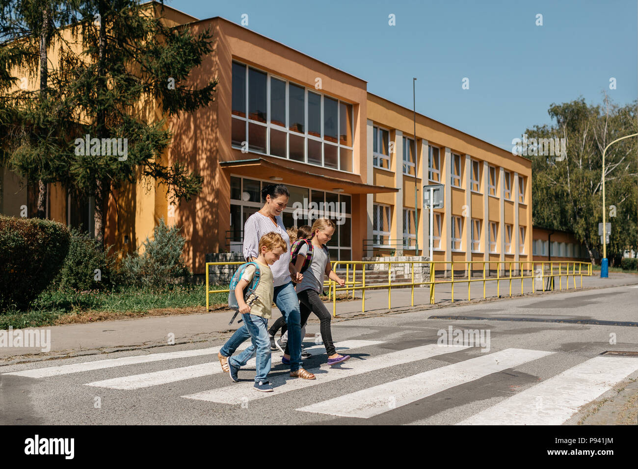 Sécurité routière - enfants traversant une route accompagné d'un adulte. Cueillette de la mère de ses enfants à l'école. Banque D'Images