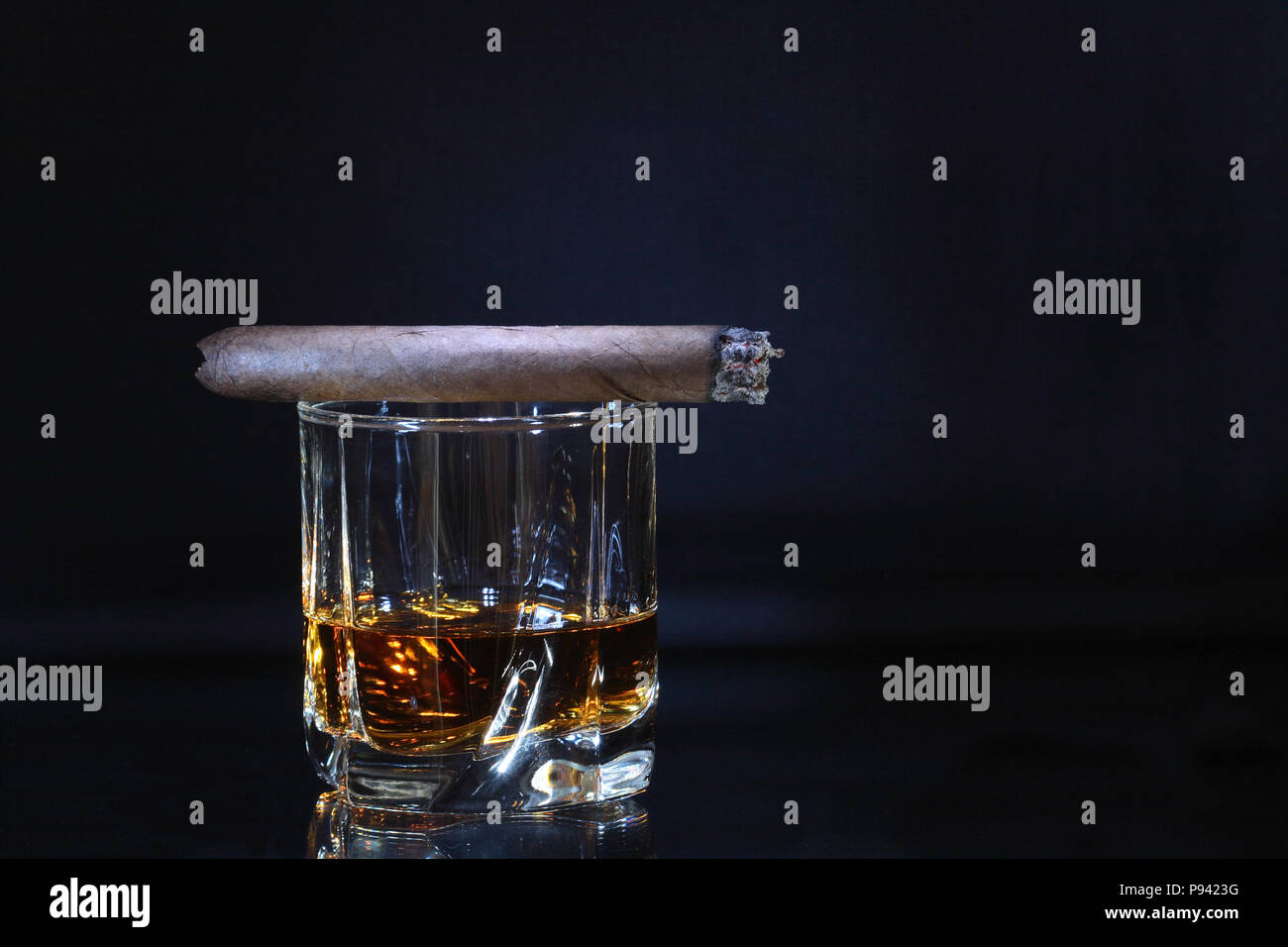 Cigare cubain couchée sur verre de whisky isolé sur fond sombre with copy space Banque D'Images