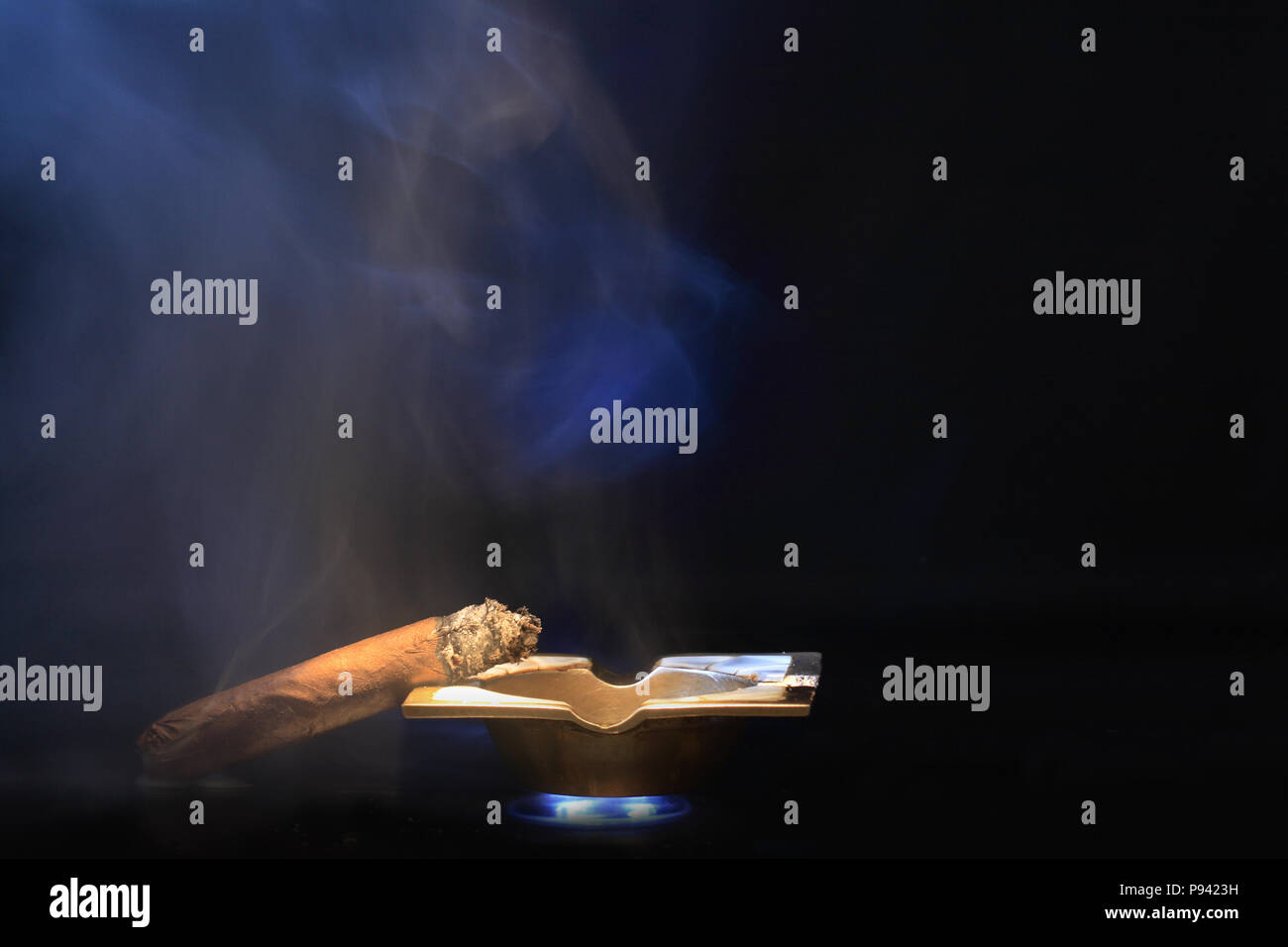Cigare cubain allongé sur le bronze ash-plateau sur fond sombre avec fumée bleue Banque D'Images