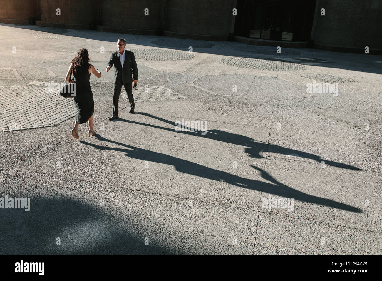 Businesswoman walking avant de serrer la main à un collègue à l'extérieur avec leurs longues ombres sur le sol. Chaque message d'autres collègues d'affaires Banque D'Images