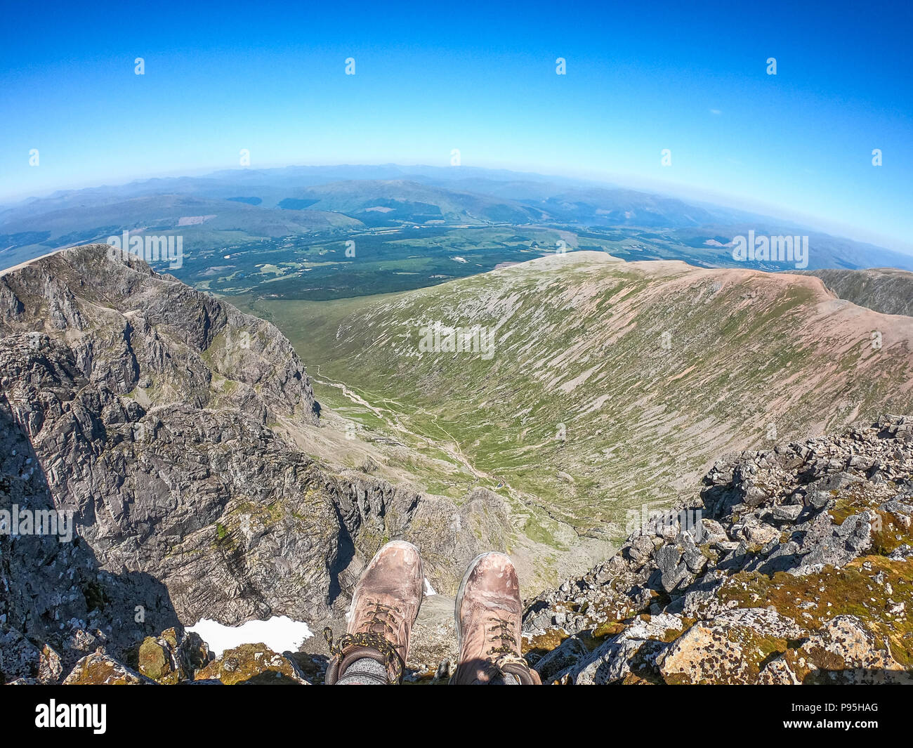 Un randonneur est assis avec les jambes pendantes sur le bord du sommet de la plus haute montagne du Royaume-Uni. Le Ben Nevis est à 1 345 mètres abov Banque D'Images
