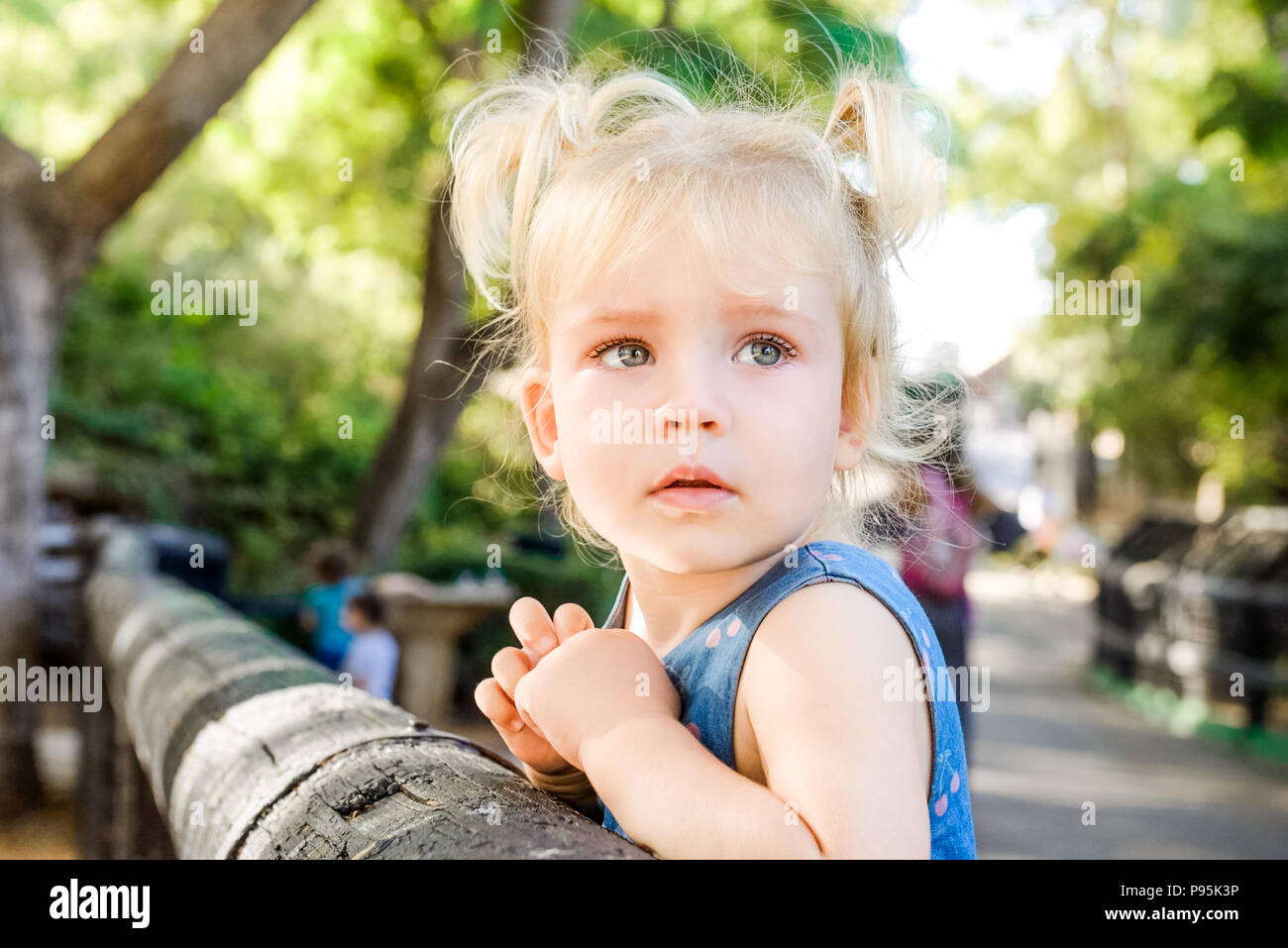 Close up portrait of cute peu désorientés blondy bébé fille à côté et s'appuyant sur une clôture en bois dans le zoo ou parc de la ville enfant , sécurité Banque D'Images