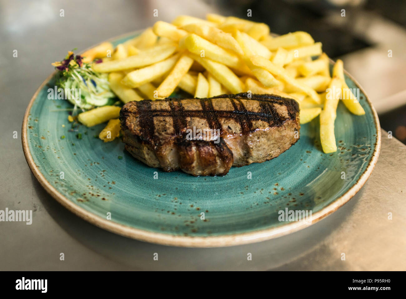 L'aloyau grillé tendre ou t-bone steak servi avec des frites dorées et salade d'herbes fraîches accompagnées d'un barbecue ou du beurre aux herbes Banque D'Images