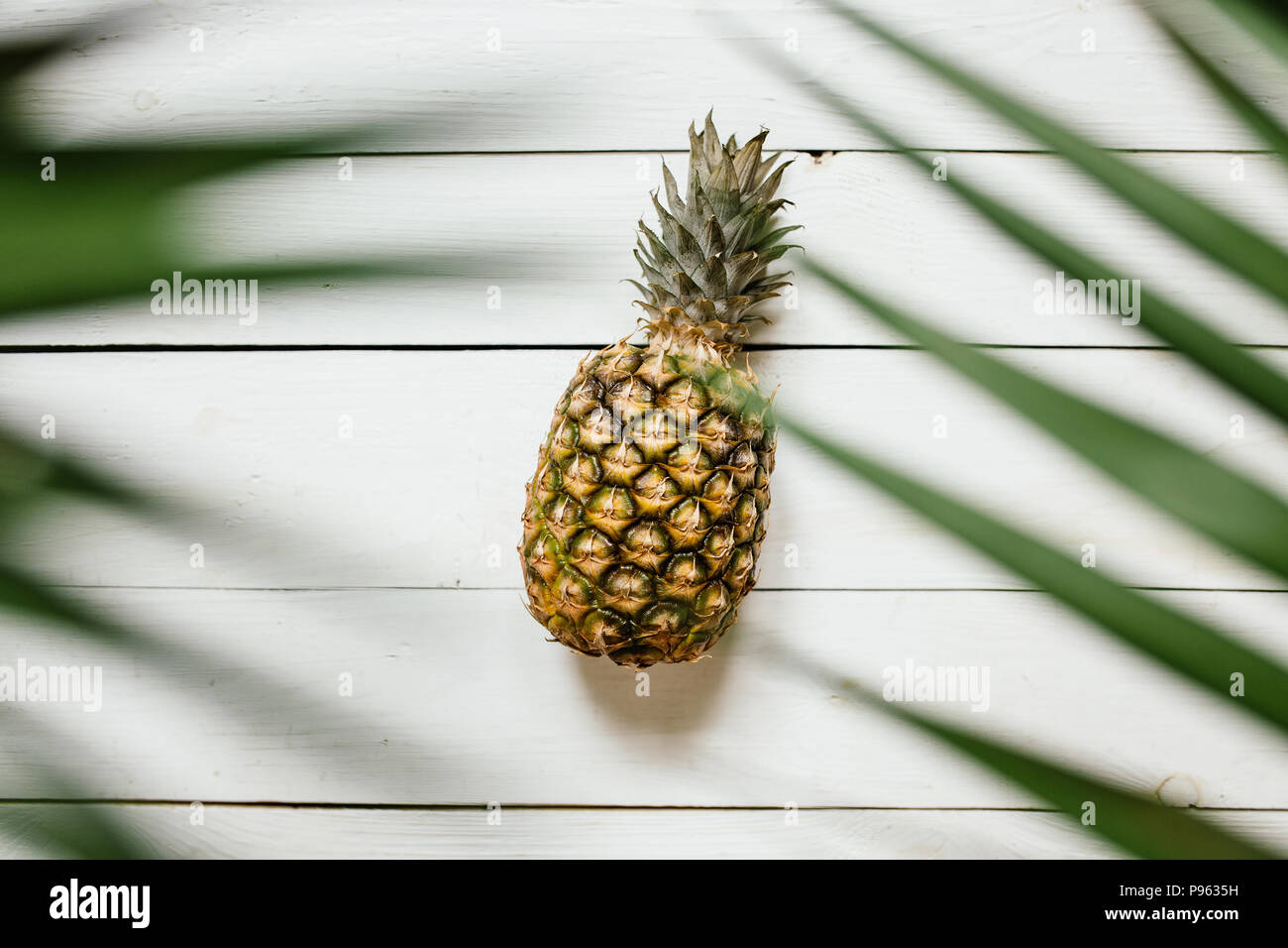 L'ananas mûr, feuilles de palmier, sur fond de bois blanc. Fruits tropicaux concept créatif. Banque D'Images