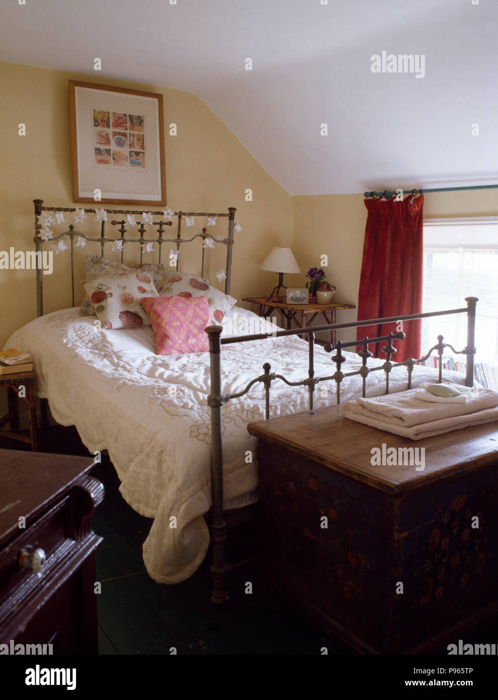 Couette blanche sur lit en laiton vintage cottage chambre avec un coffre en bois peint au pied du lit Banque D'Images