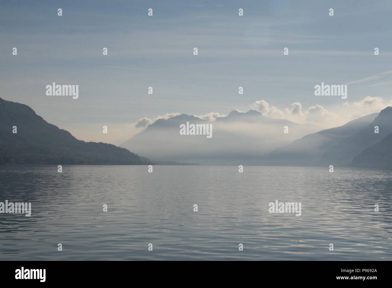 Vue sur le lac de Côme vers les montagnes avec les nuages planant au-dessus des montagnes et de la brume sur le lac de séance. Banque D'Images