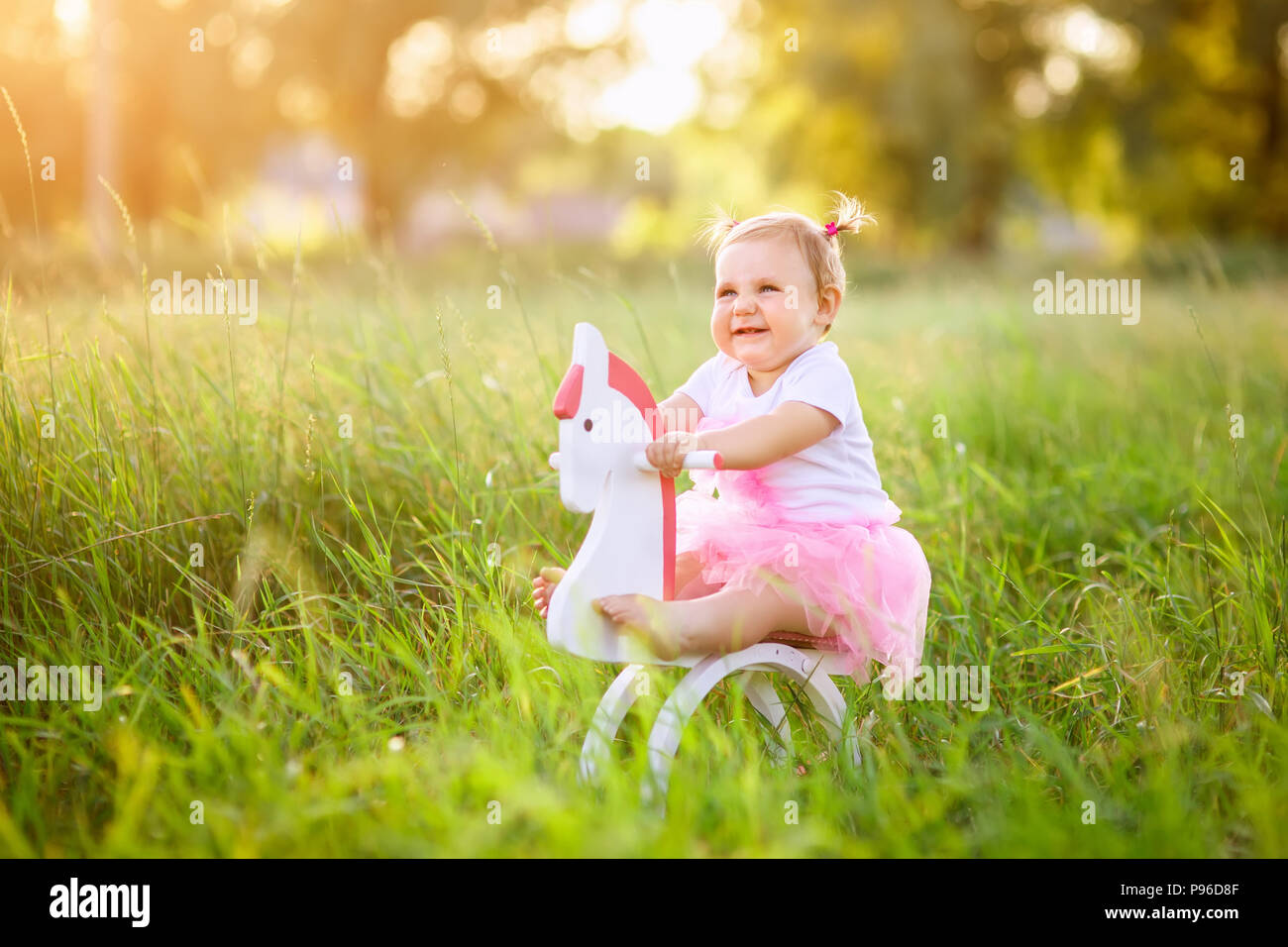 Belle petite fille en robe rose équitation sur cheval jouet en bois à l'extérieur Banque D'Images