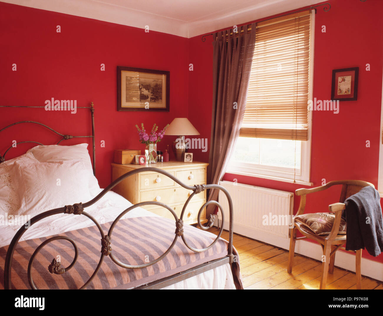 Lit en fer forgé décoré en rouge petite chambre avec fenêtre au rideau  beige avec sommier à lattes aveugles en bois Photo Stock - Alamy