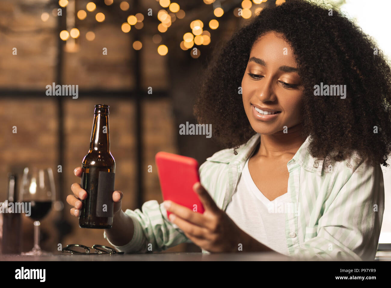 Superbe femme bouclés boire de la bière et à l'aide de Phone Banque D'Images