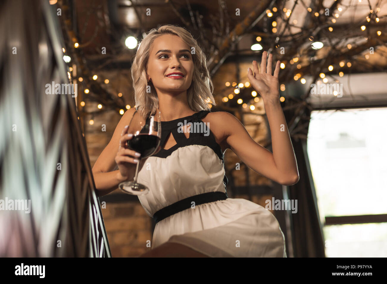 Jolie femme blonde boire du vin et en agitant à quelqu'un Banque D'Images