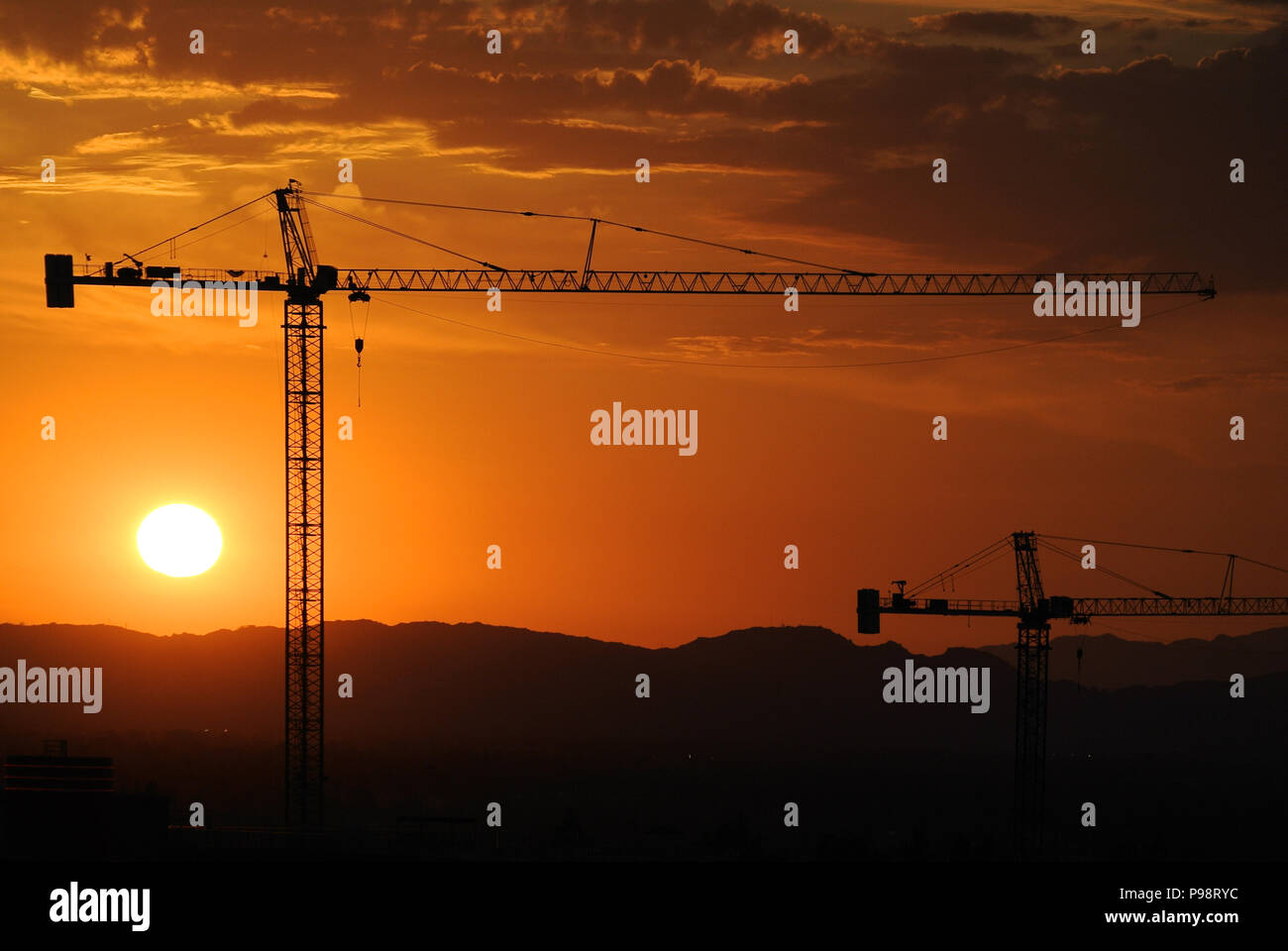 Silhouette de deux grues de construction au coucher du soleil Banque D'Images