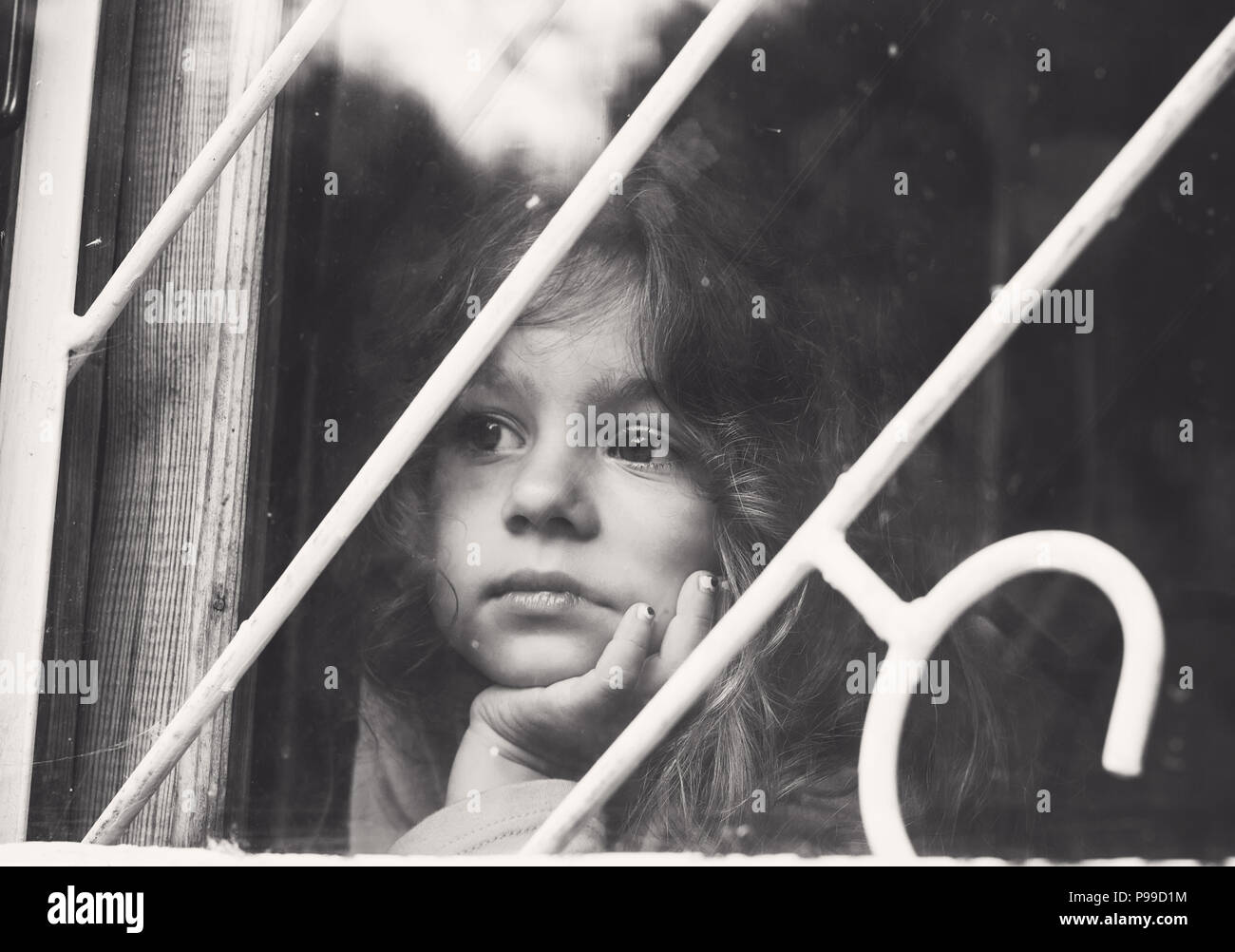Portrait noir et blanc de triste petite fille regarde par la fenêtre en treillis Banque D'Images