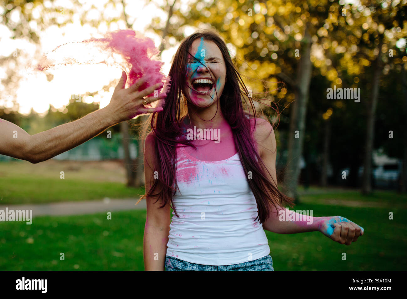 Femme en riant parc alors que ami masculin de jeter de la poudre de couleur sur son visage. Amis jouant avec holi festival au parc. Banque D'Images