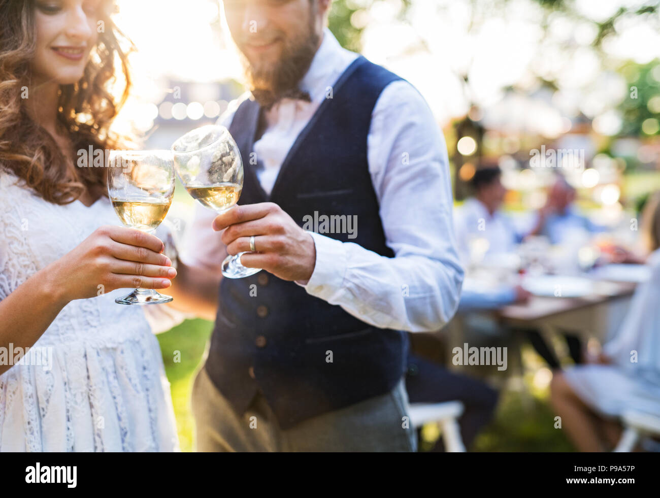 Bride and Groom clinking glasses at Wedding Reception à l'extérieur dans la cour. Banque D'Images
