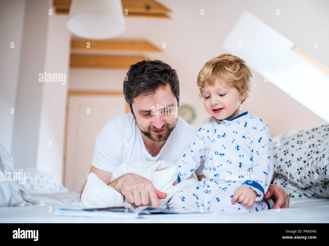 Père avec bébé garçon la lecture d'un livre sur le lit chez lui à l'heure du coucher. Banque D'Images