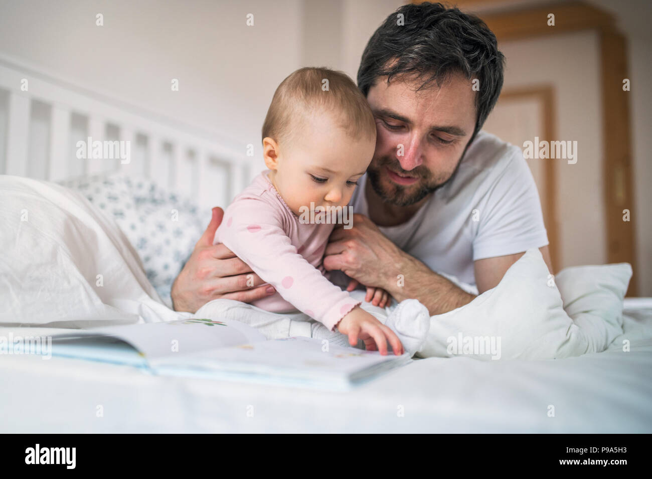 Père avec bébé fille lire un livre sur le lit chez lui à l'heure du coucher. Banque D'Images