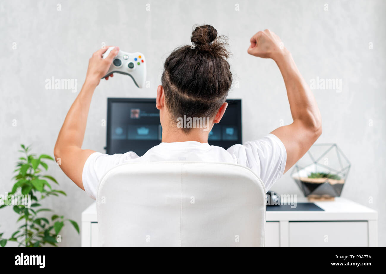 Heureux jeune homme jouant et gagnant jeu en ligne sur ordinateur. Vue arrière de la console vidéo avec manette. Jeux de compétition, de l'électronique Banque D'Images