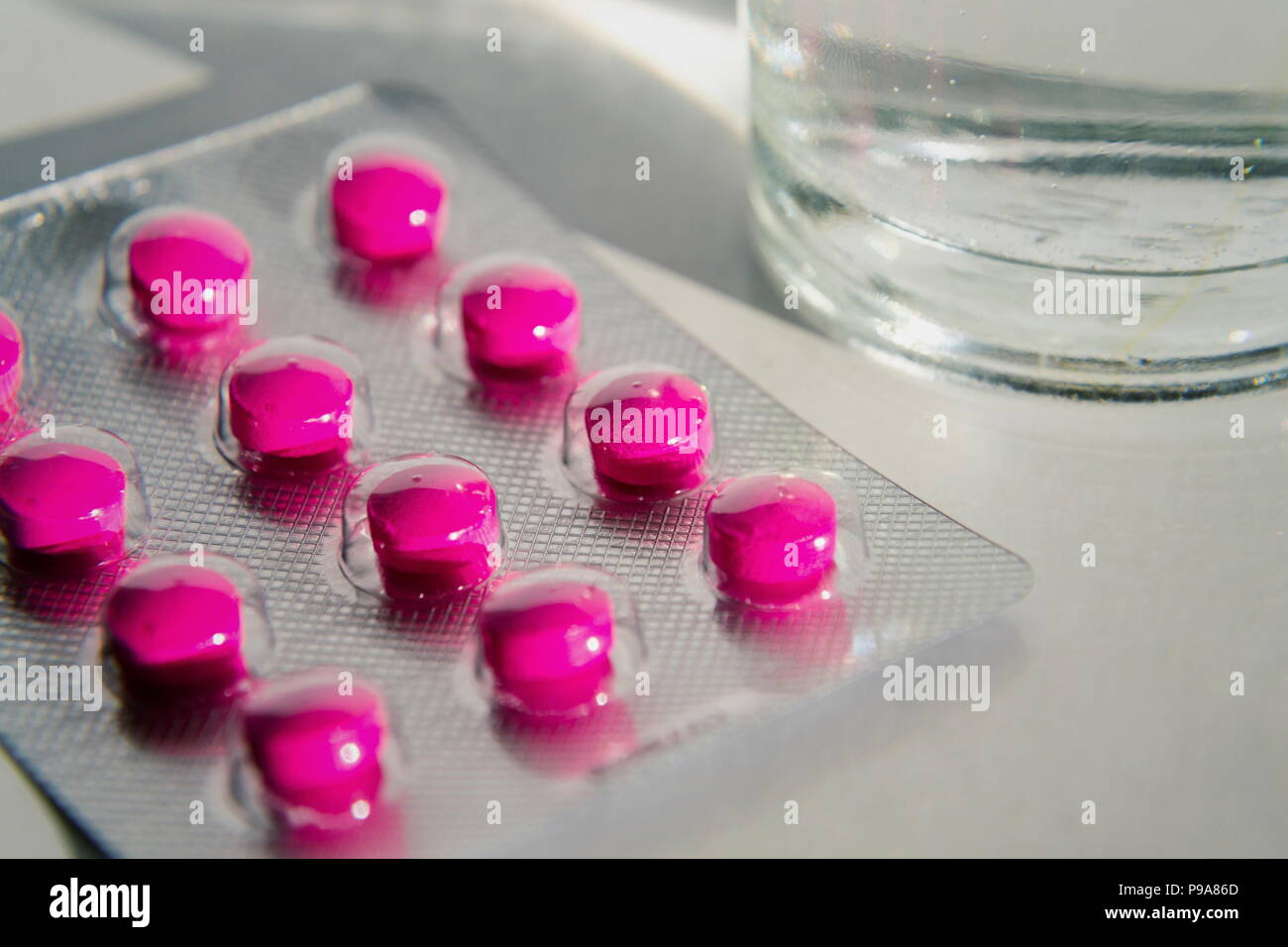 Pilules roses avec verre d'eau isolé sur fond blanc Banque D'Images