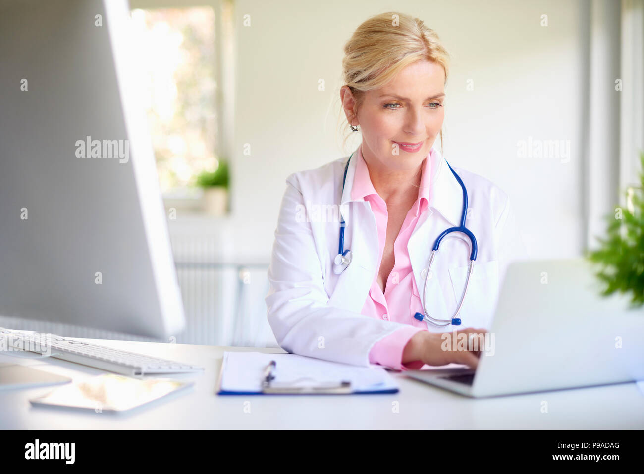 Femelle adulte médecin en utilisant son ordinateur portable tout en étant assis au bureau du médecin. Banque D'Images