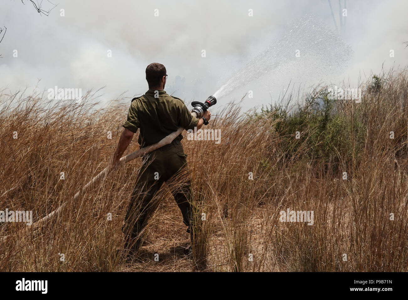 Conseil Régional Eshkol, Israël. 17 juillet, 2018. Les pompiers, le KKL forest rangers et des soldats combattre côte à côte pour éteindre un feu de forêt à l'ouest du kibboutz Beéri, dans le conseil régional Eshkol, près de la bande de Gaza, enflammé par des bombes incendiaires et explosifs livrés par les cerfs-volants ou des ballons gonflés à l'hélium de la bande de Gaza en Israël. Plus de 50 kilomètres carrés de champs agricoles et forestières ont été incendiés dans une vague d'incendies criminels, le terrorisme palestinien maintenant dans son quatrième mois. Credit : Alon Nir/Alamy Live News Banque D'Images