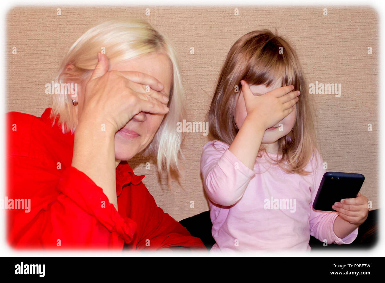 Belle blonde jeune grand-mère et petite-fille cute peu fermer les yeux avec les mains Banque D'Images