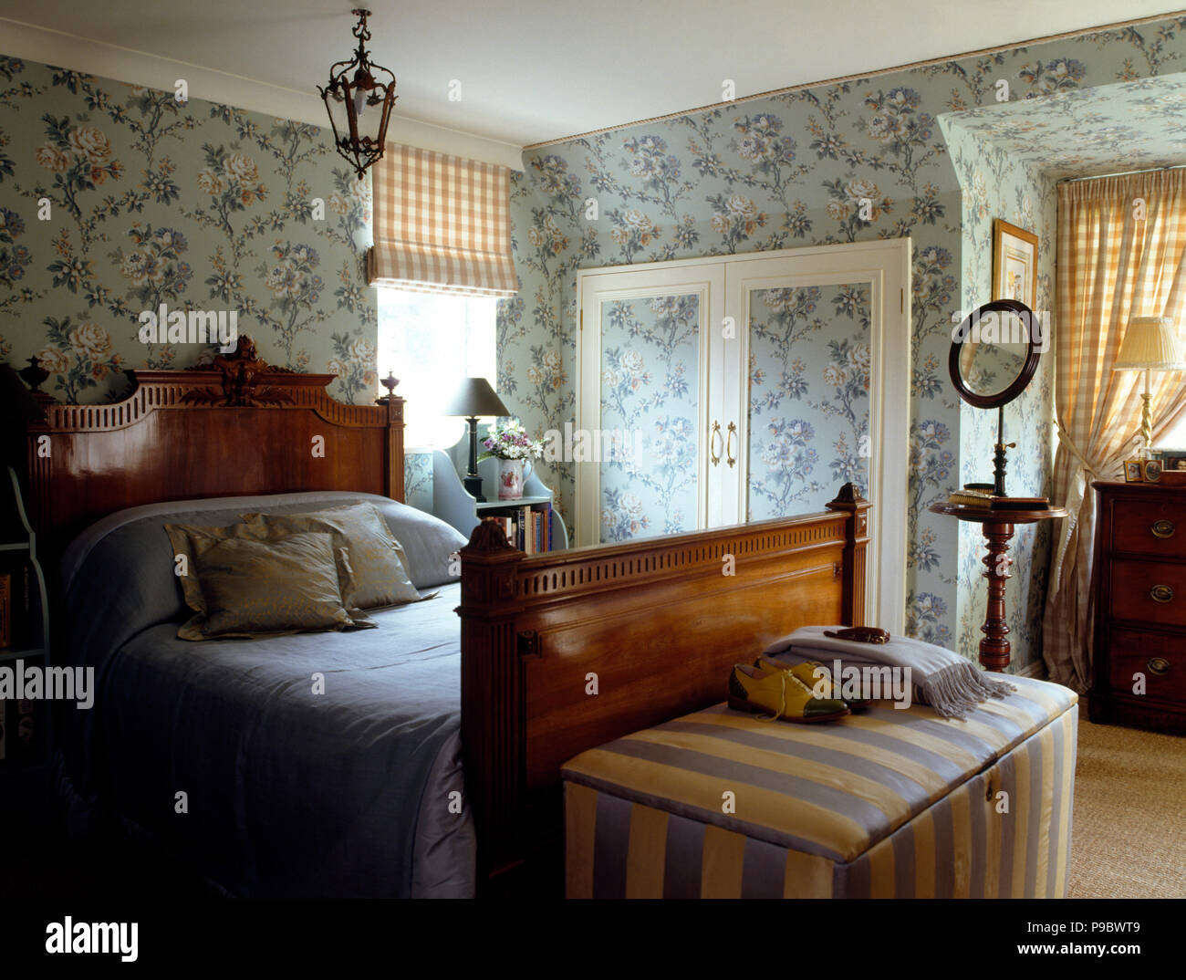 Ottoman rayé au pied d'un lit d'époque dans une maison de chambre avec un papier peint fleuri bleu Banque D'Images