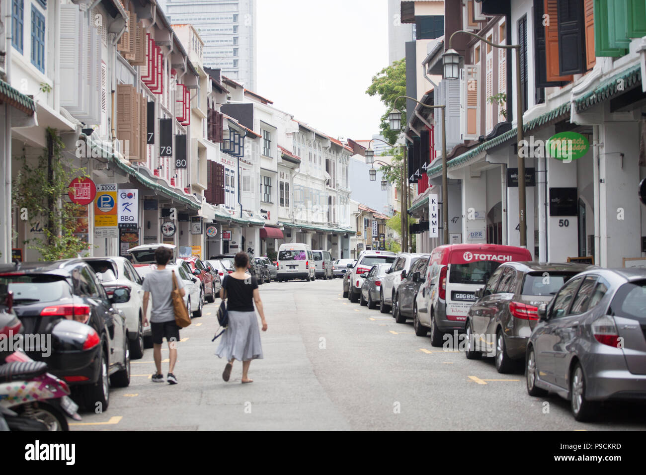 Deux touristes marchant sur la route avec des magasins conservés de chaque côté. Singapour. Banque D'Images