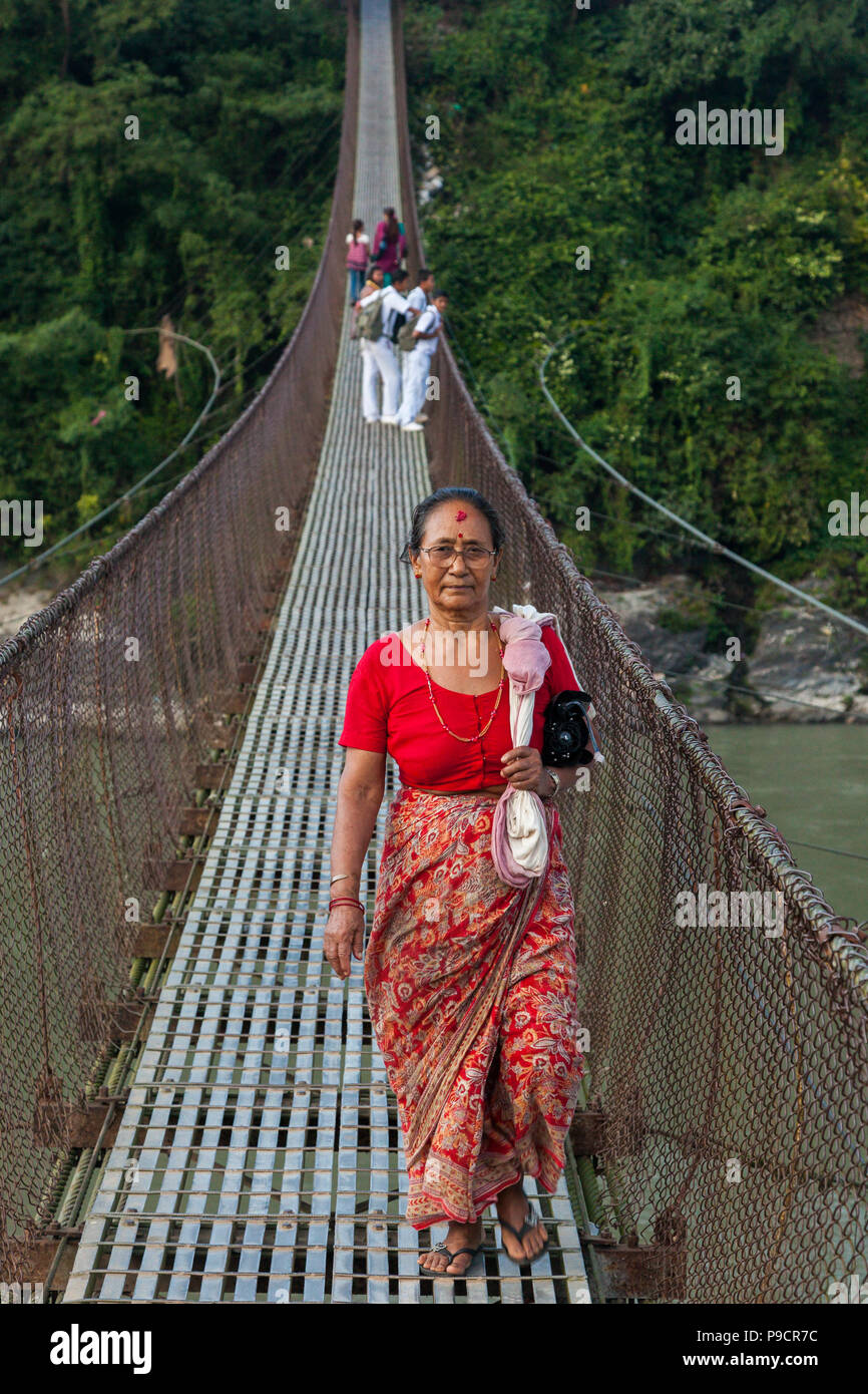 Femme traversant une rivière sur un pont suspendu au Népal Banque D'Images