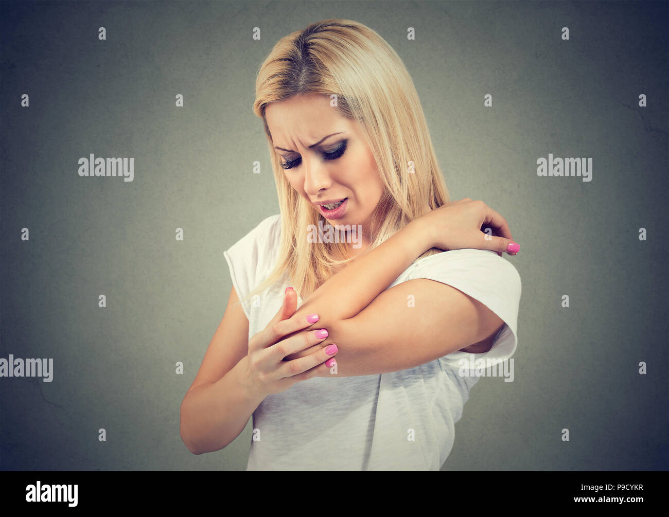 Hot woman in Casual t-shirt froncer de douleur après avoir traumatisme de coude sur fond gris Banque D'Images