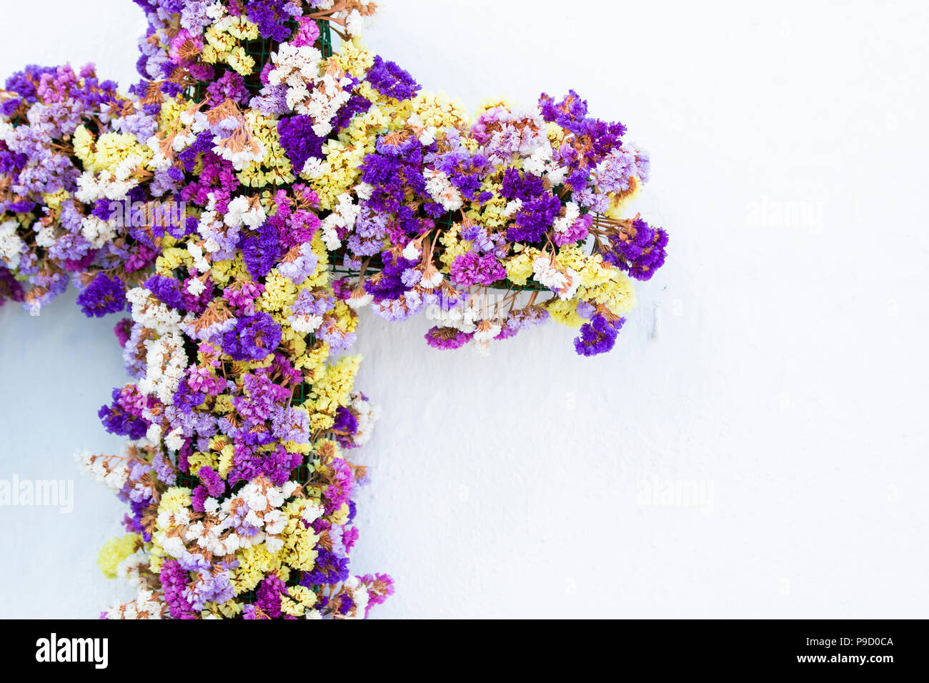 Croix incroyable décorées de petites fleurs multicolores accroché sur un mur de plâtre blanc Banque D'Images