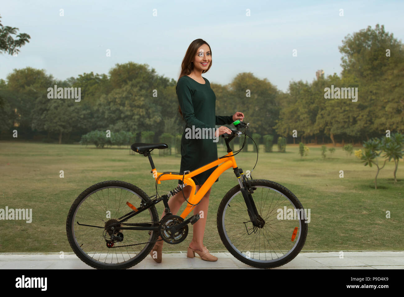 Smiling young woman in park with bicycle Banque D'Images