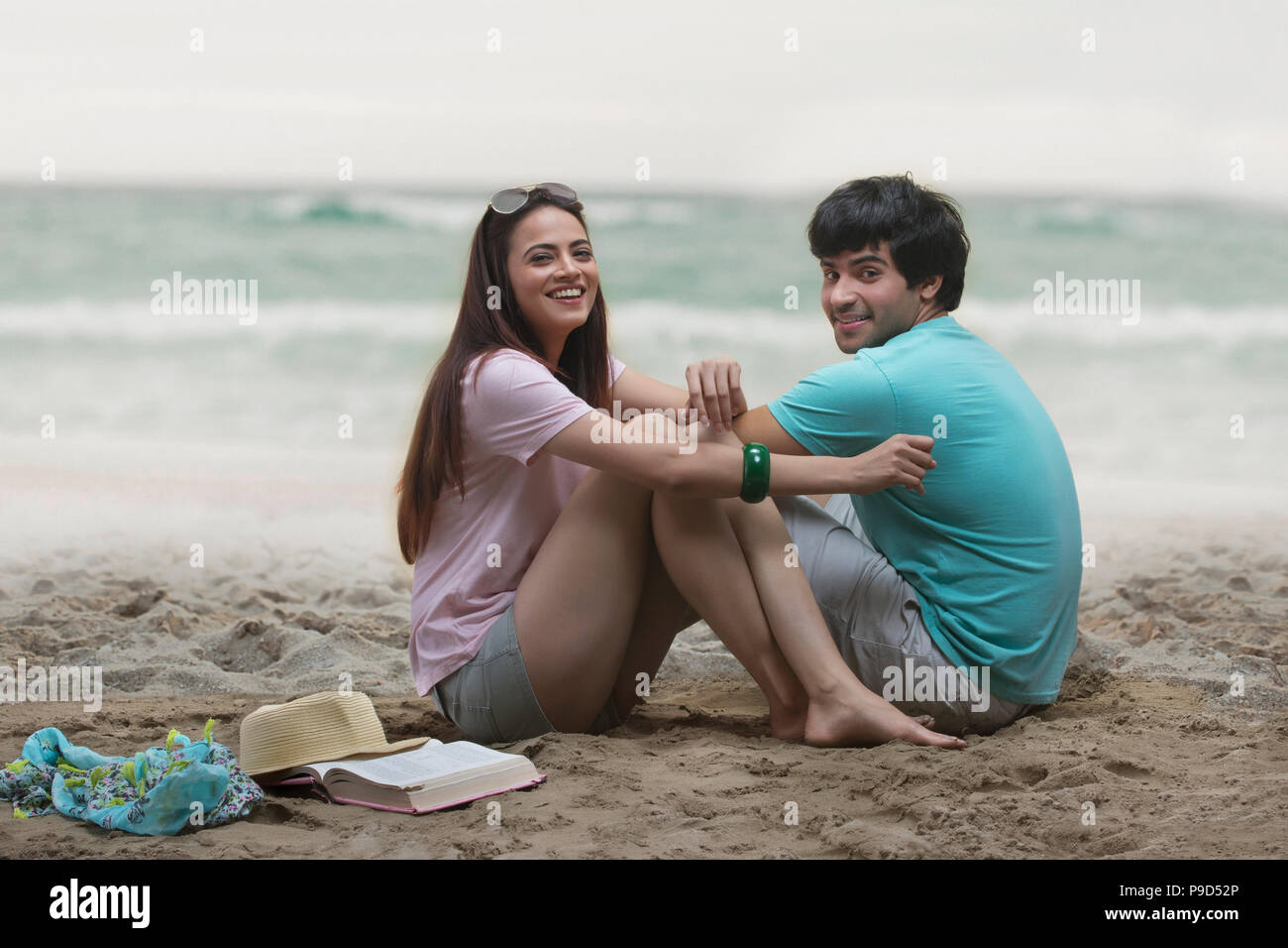 Smiling young couple sitting on beach Banque D'Images