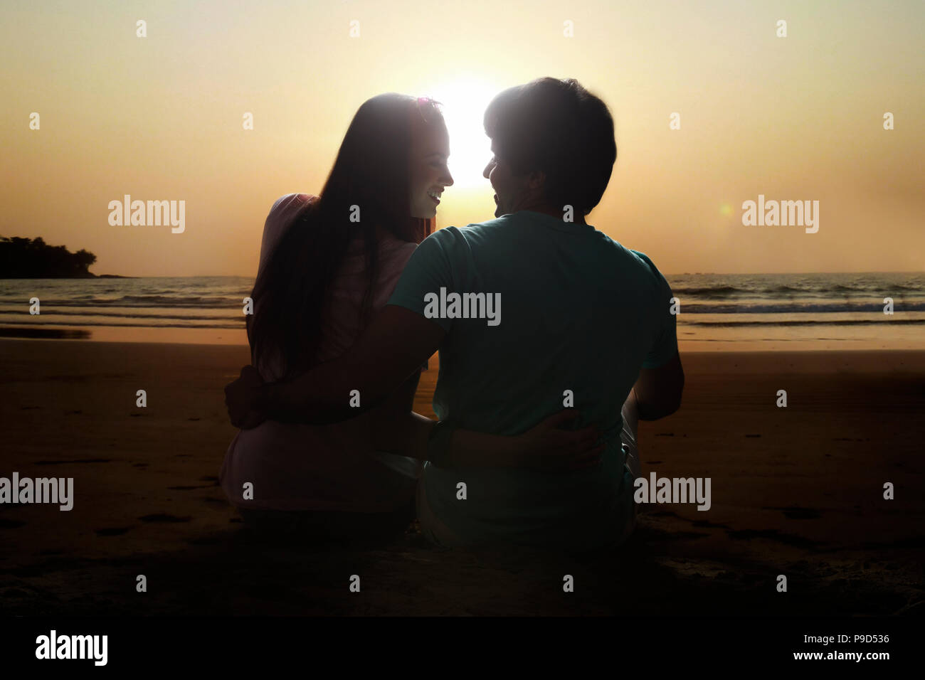 Young couple sitting on beach at sunset Banque D'Images