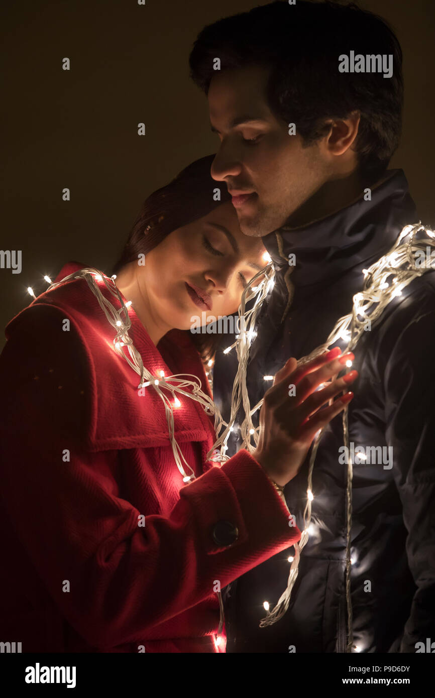 Jeune couple romantique enveloppée dans des lumières décoratives Banque D'Images