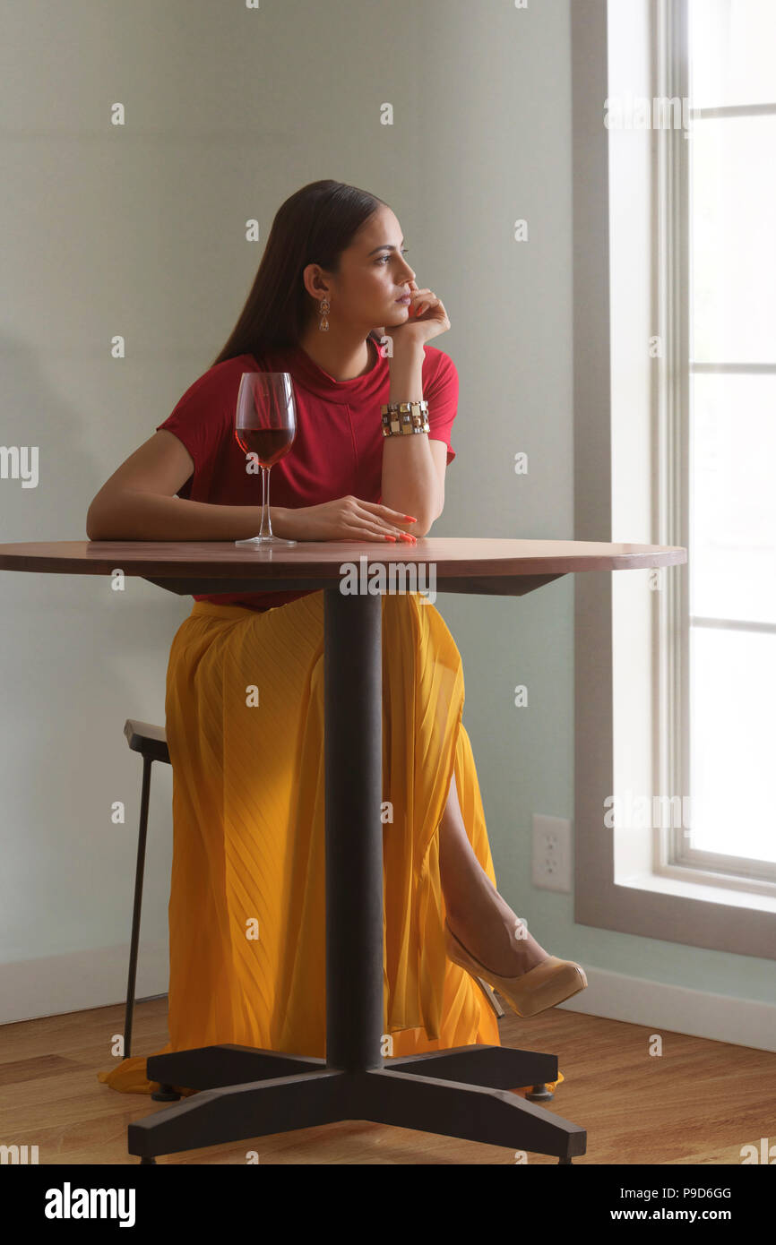 Jeune femme assise à table avec verre de vin Banque D'Images
