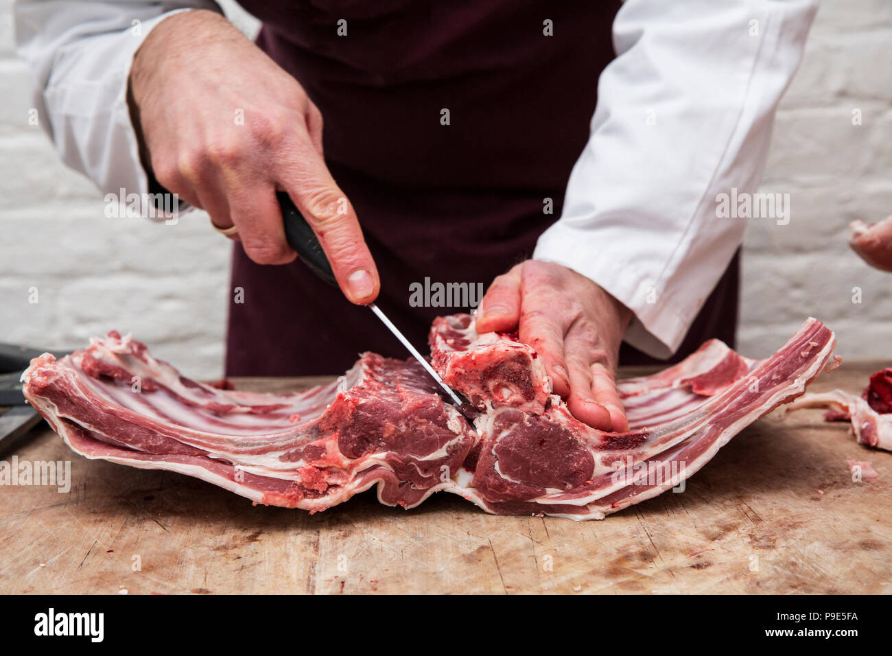 Un boucher à l'aide d'un couteau bien aiguisé pour préparer les côtes d'agneau pour le carré d'agneau. Banque D'Images